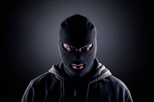 Criminal wearing black balaclava and hoodie in the dark Image of a thief